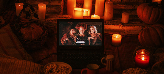 A cozy scene of a candlelit room, with bowls of popcorn, mugs (cocoa? tea?) and a laptop showing the movie 'Hocus Pocus'.