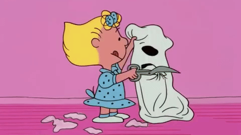 Sally from The Peanuts cutting eyeholes in a white sheet to use as a ghost costume